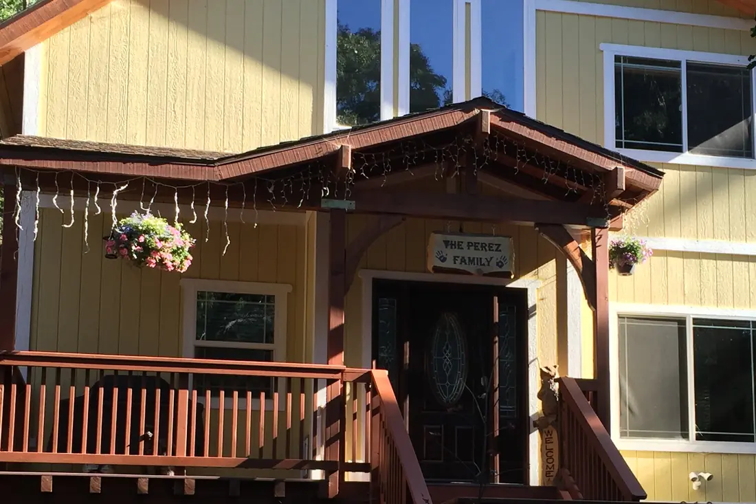 A mountain home entry with a stained redwood pergola and railings against pale yellow siding
