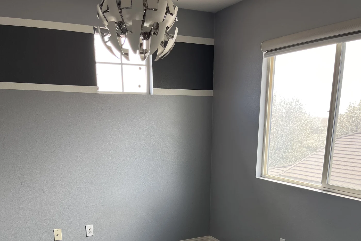 A room painted soft gray with a charcoal band and white pinstripes running around the top of the walls, beside a window