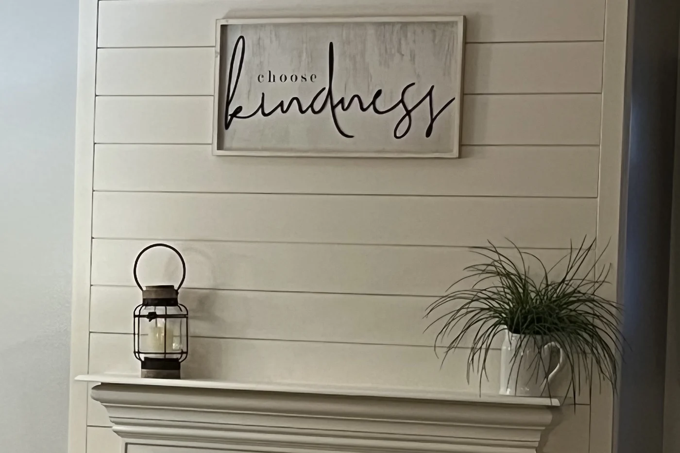 A white shiplap fireplace wall with a painted mantel and a framed sign hung above it