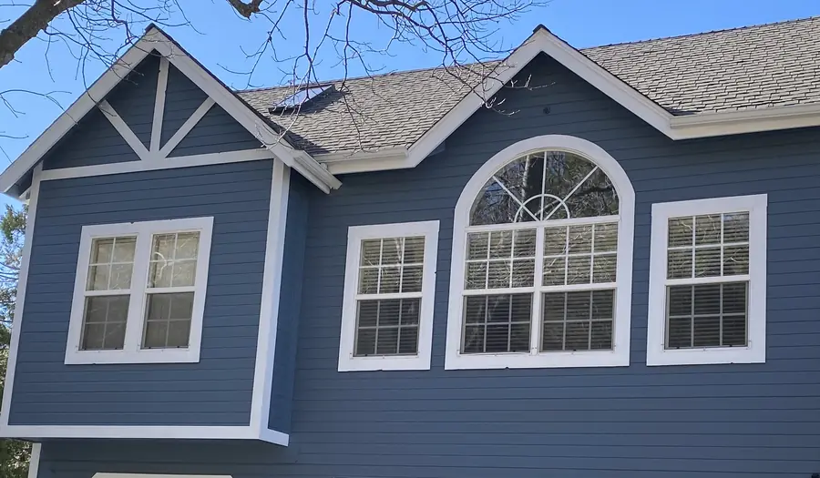 Slate-blue siding with crisp white trim around a gable and arched window, after an exterior repaint
