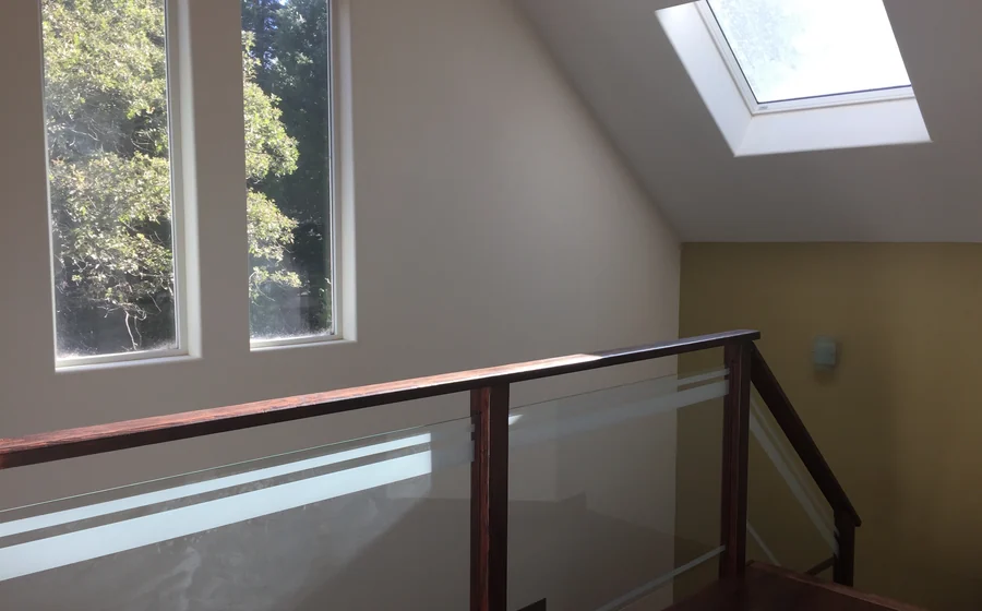 An upstairs landing painted in white and soft olive, lit by a skylight, with a stained wood and glass railing