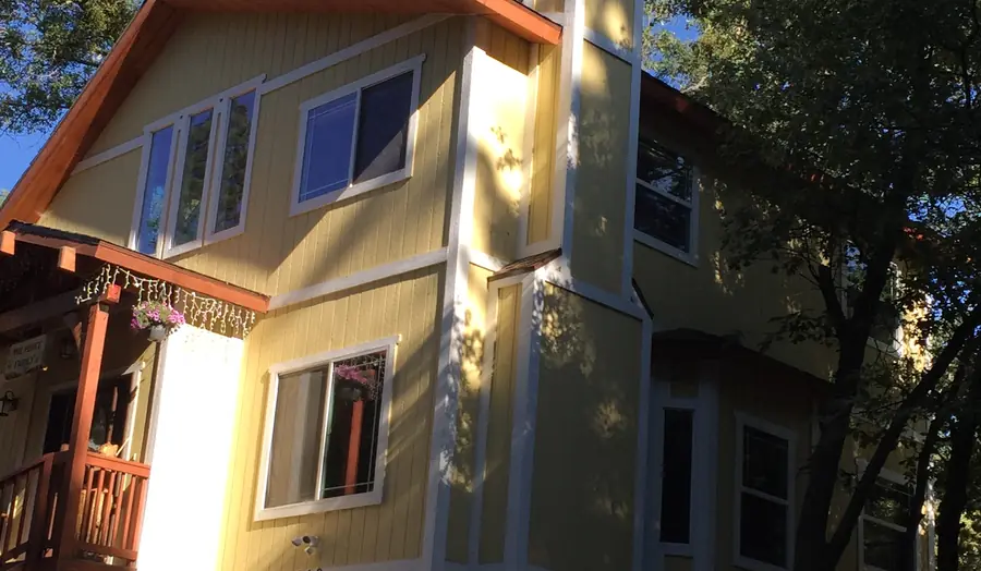 A repainted mountain home in pale yellow with white trim and redwood posts